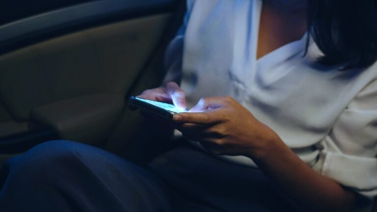 A person sitting in a dimly lit room holding a glowing smartphone, suggesting suspense or mystery. Image for an A2 ESL lesson from betterclass titled Scary Story in Messages, where students explore spooky sounds, read text message stories, and create their own Halloween endings.
