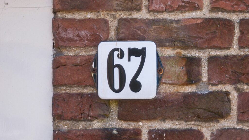 A close-up of a house number plate reading “67” on a brick wall. Image for the What Does 67 Even Mean ESL lesson from betterclass, exploring viral internet trends, online humor, and digital culture through discussion and vocabulary activities.