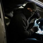 Masked car thief sitting in a vehicle at night, representing Britain’s stolen car market and used to illustrate an ESL lesson on global crime and trade.