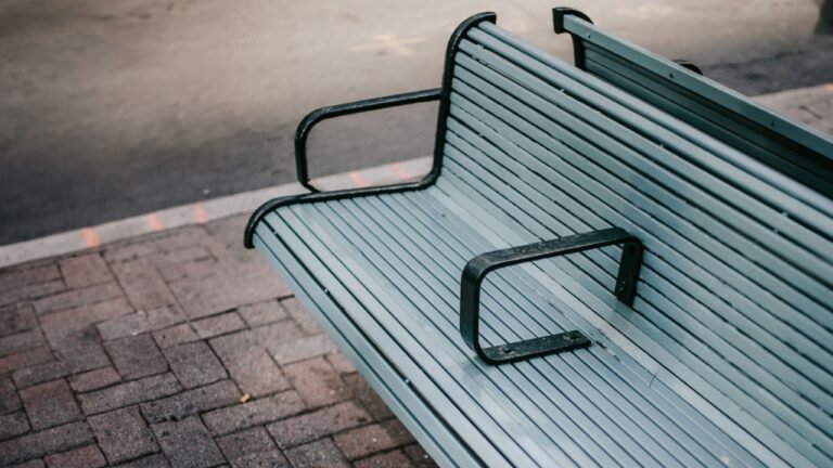 A modern city bench with metal arm dividers, symbolizing hostile architecture and exclusion in urban design.