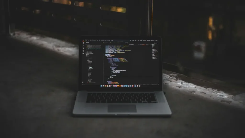 A laptop displaying lines of code in a dark environment. The image connects to the ESL lesson title “Vibe Coding” – Word of the Year by visually representing the concept of “coding” while symbolizing creativity, focus, and modern digital culture — themes explored in the lesson about language trends and tech-inspired expressions.