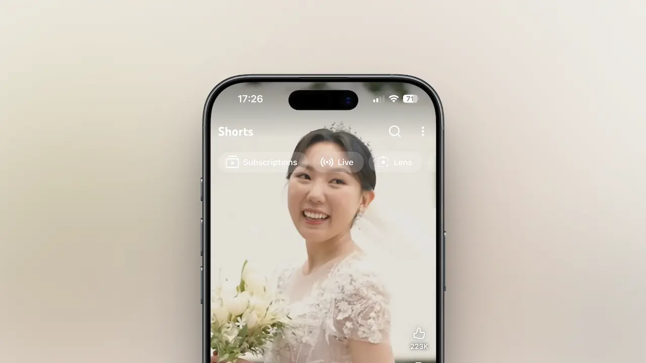 A smartphone screen showing a smiling bride in a white wedding dress holding a bouquet. The image appears on a video app interface. This image connects to the A2 ESL lesson about weddings and technology by showing how people today watch short videos of weddings online. It supports vocabulary and discussion about modern weddings, Korean culture, and how social media changes wedding traditions.