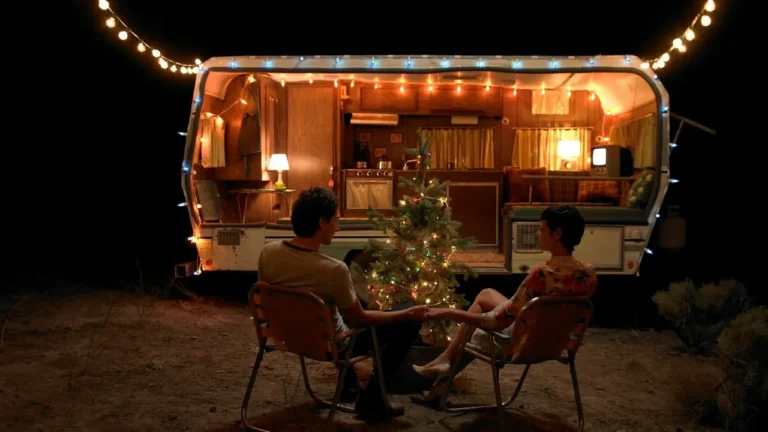 Couple sitting by Christmas tree in front of illuminated camper van at night - cozy holiday romantic scene for ESL lesson