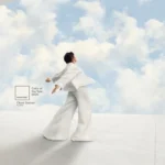 A person wearing a flowing white outfit stands against a sky background with billowing clouds, with a Pantone label showing 'Color of the Year 2026 Cloud Dancer 11-4201' displayed in the image.