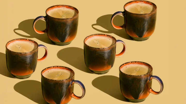 Five ceramic coffee mugs with green glaze and foam on beige background for ESL lesson about coffee drinks and café vocabulary