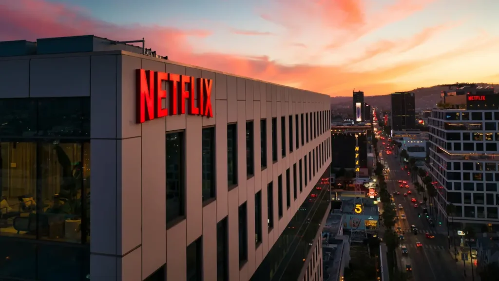 Netflix headquarters building with illuminated red logo sign at sunset, overlooking a busy city street with traffic and surrounding buildings during golden hour.