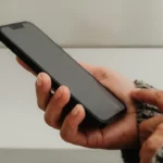 Hand holding a smartphone with a blank screen against a neutral background, suggesting mobile apps, digital communication, or modern tech use.