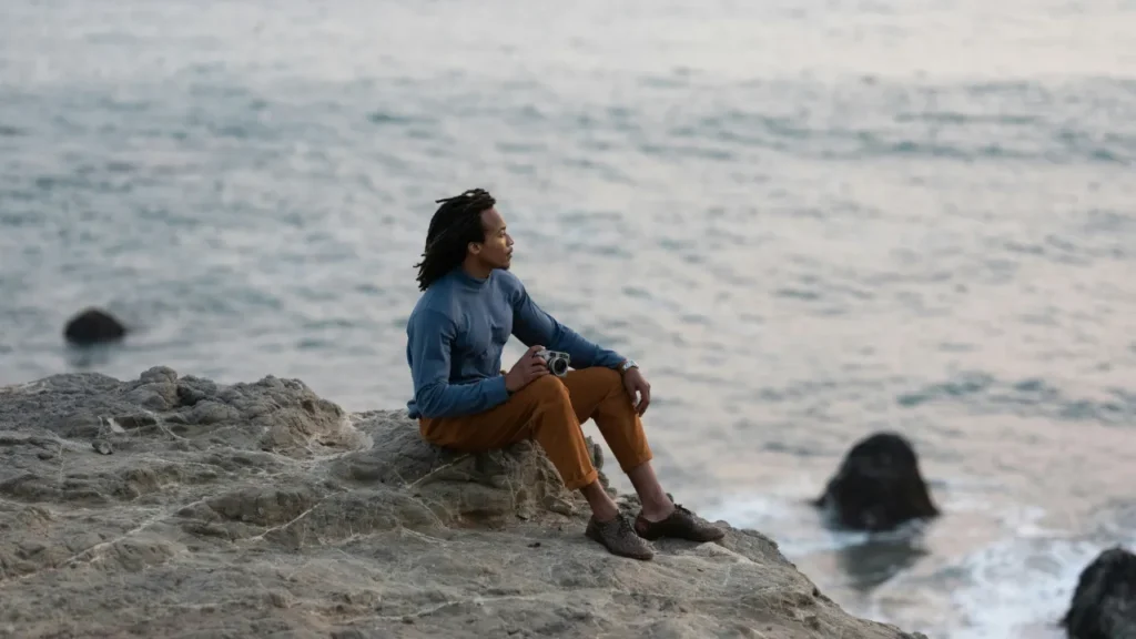 A solitary figure sits on seaside rocks overlooking the ocean, symbolizing modern singlehood and independence
