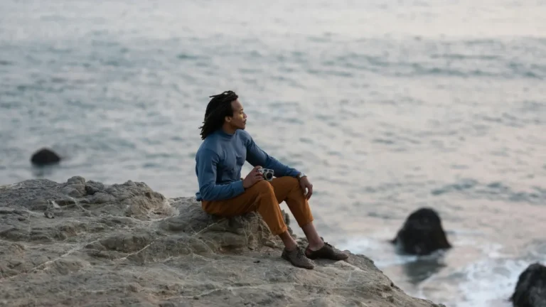 A solitary figure sits on seaside rocks overlooking the ocean, symbolizing modern singlehood and independence