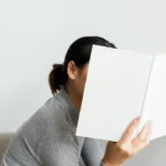 A woman hiding behind a book, representing the need to switch off from work in a B2 English lesson plan about work-life balance