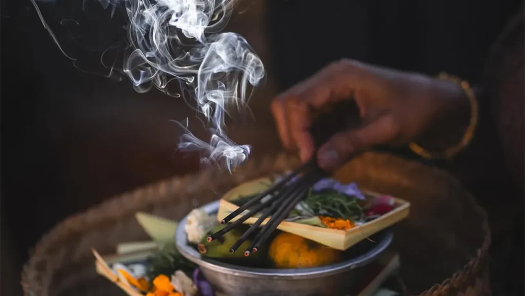 Burning incense with white smoke above a spiritual altar arrangement of colorful flowers and botanicals