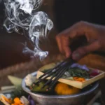 Burning incense with white smoke above a spiritual altar arrangement of colorful flowers and botanicals