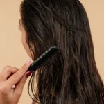 B1 English lesson plan on getting a haircut — woman combing long wet dark hair after washing, beige background.