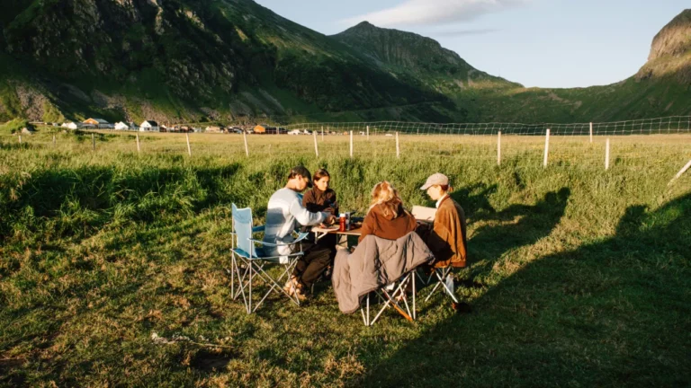 Four friends eat together outdoors in a mountain valley — a cover image for an A2 vacation lesson about countryside travel.