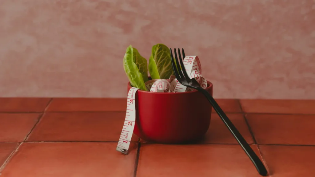 A red bowl with lettuce leaves, a fork, and a measuring tape. C1 lesson plan on weight loss, genetics, and GLP-1 drugs like Zepbound.