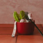 A red bowl with lettuce leaves, a fork, and a measuring tape. C1 lesson plan on weight loss, genetics, and GLP-1 drugs like Zepbound.