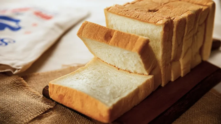 Sliced white sandwich bread on a wooden board, with a branded plastic bag visible in the background.