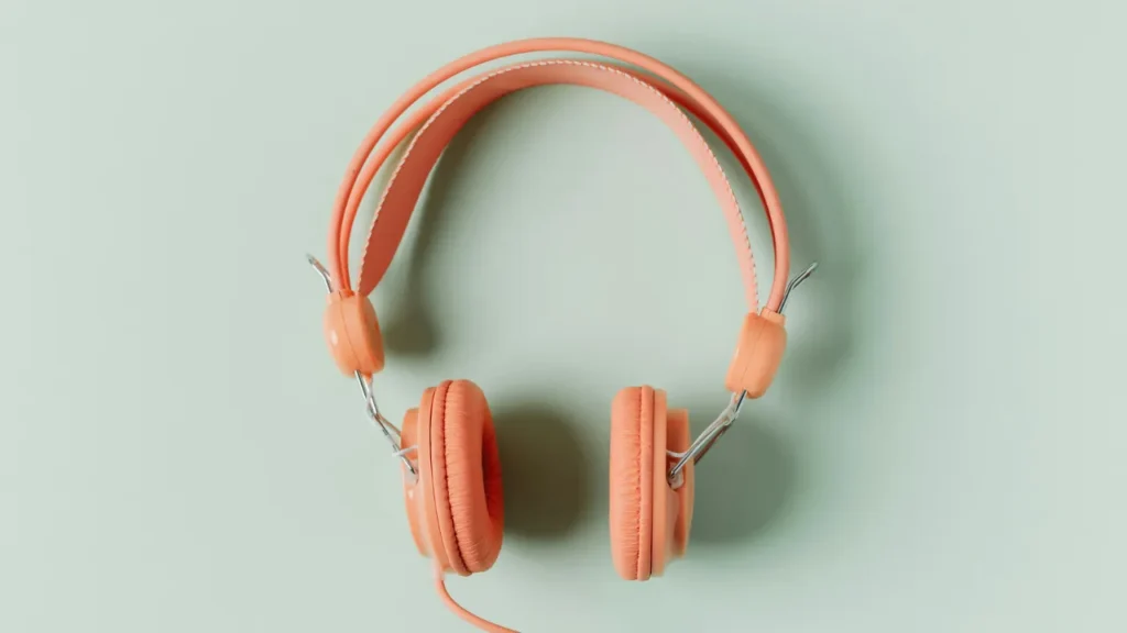 Coral-colored wired headphones on a mint green background, viewed from above
