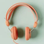 Coral-colored wired headphones on a mint green background, viewed from above