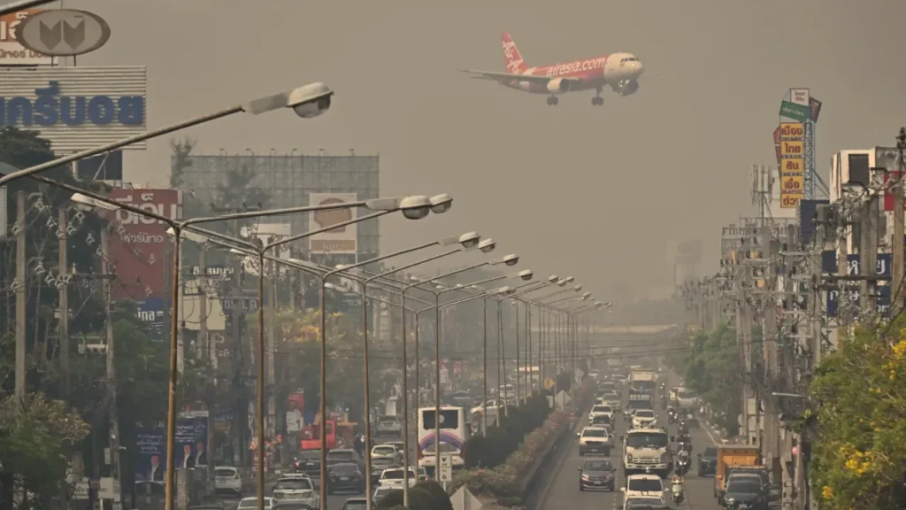 A smog-filled street in Chiang Mai, Thailand, with an AirAsia plane flying through hazy grey air.