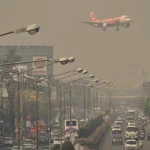 A smog-filled street in Chiang Mai, Thailand, with an AirAsia plane flying through hazy grey air.