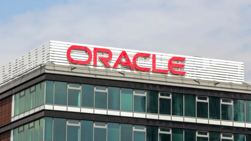 Oracle company building with large red logo sign on glass facade against a blue sky.