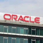 Oracle company building with large red logo sign on glass facade against a blue sky.
