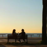 Two people sitting on a bench by the sea at sunset, deep in conversation — B2 lesson plan on asking meaningful questions.
