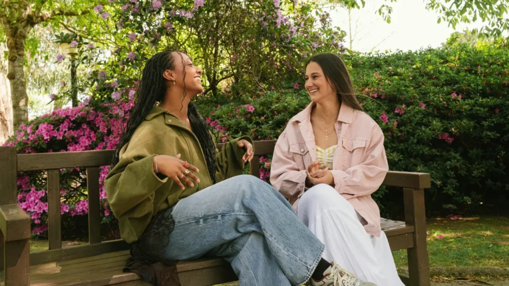 Two friends talking and smiling on a bench outdoors, used in a giving compliments A2 lesson plan for adult ESL learners.