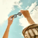 8:10 PM Person holding sunglasses up toward a bright summer sky, used in a C1 lesson plan on how to have a great summer.