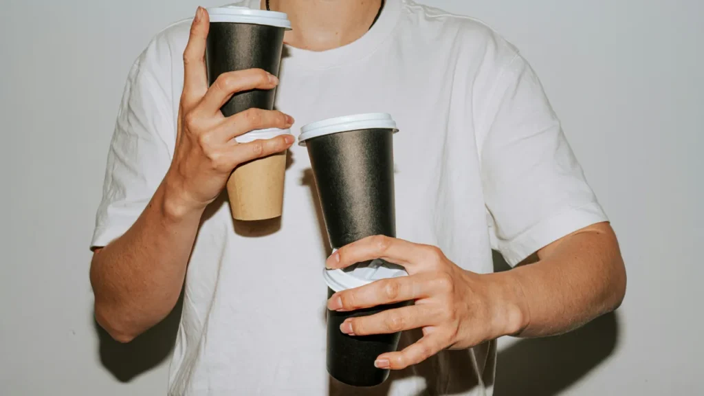 Person holding three takeaway coffee cups at once, illustrating caffeine dependency in a C1 lesson plan on quitting coffee.