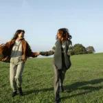 Two young women holding hands and laughing in a green field on a sunny day. A2 lesson plan friends.
