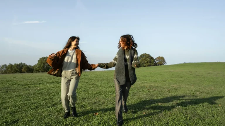 Two young women holding hands and laughing in a green field on a sunny day. A2 lesson plan friends.